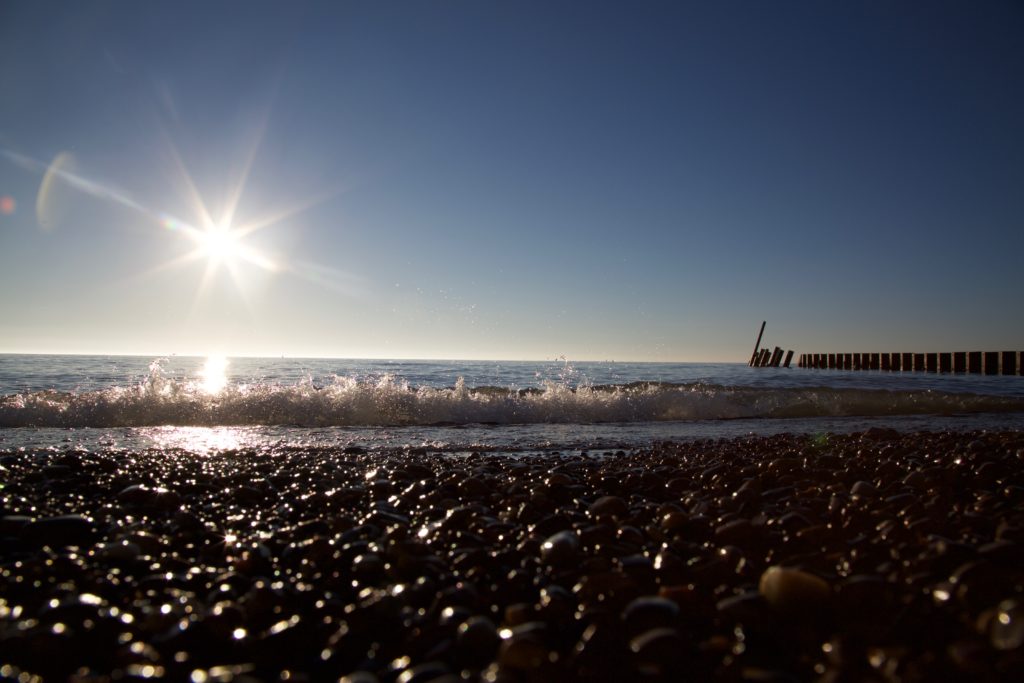 bright sun, blue sky, water, stones on the beach 